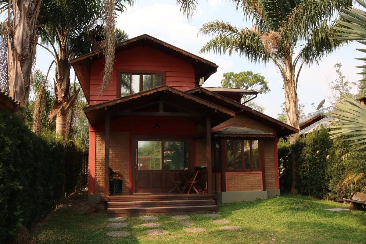 Una casa de dos pisos con fachada roja, un porche delantero y un pequeño jardín.