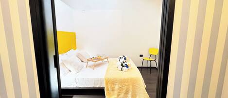Habitación de hotel con cama, una mesita con una bandeja de comida, una silla y cabecera amarilla.