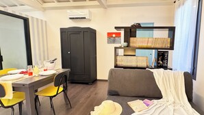 Ein gemütlicher Raum mit Esstisch für vier Personen, einer Couch, einem Bücherregal und einem Kleiderschrank.