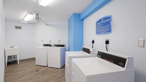 A laundry room with three washing machines, a sink, and a blue wall sign. - Rare Walkout Unit With Private Staircase to Pool/beach (Marco Island)