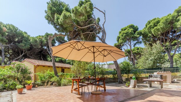 Un patio al aire libre con una mesa y sillas de madera, una sombrilla y plantas en macetas.