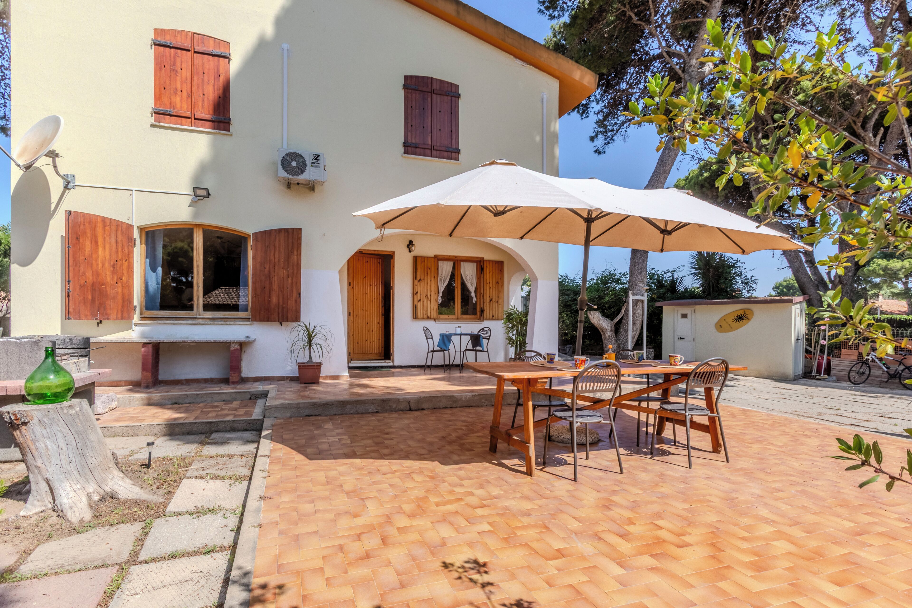 Een huis met een patio, compleet met een tafel en stoelen onder een grote parasol, een schotelantenne en houten luiken.