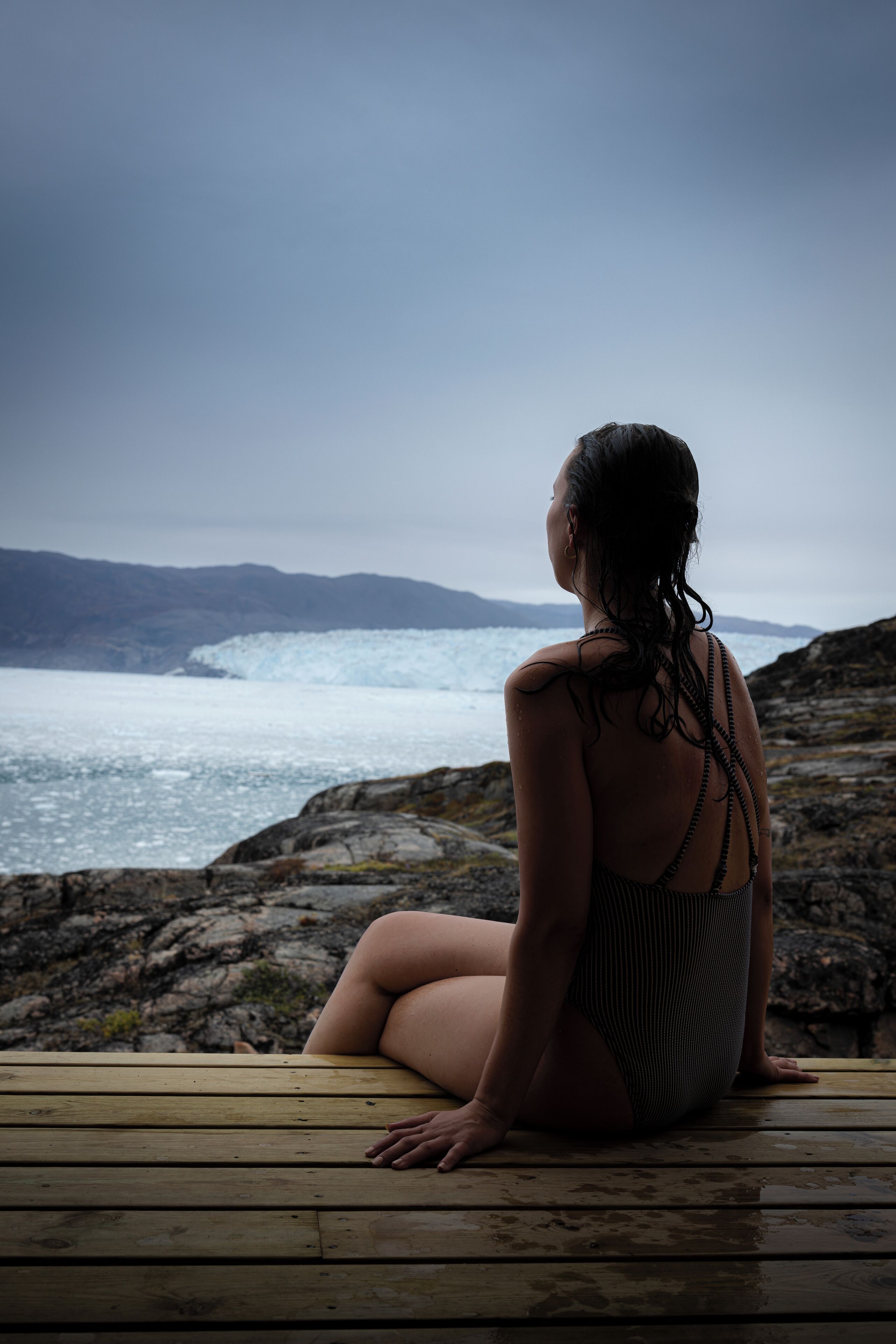 A person sitting on a wooden deck overlooking a glacier and ocean.
