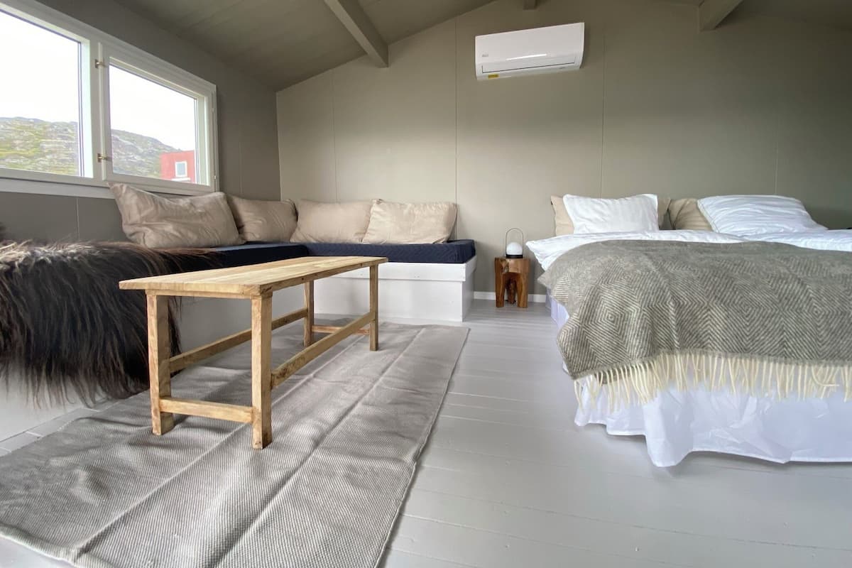 A bedroom with a bed, a wooden table, a bench, and a window.