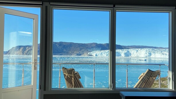 A room with large windows offering a view of a glacier and mountains. - Eqi Glacier Lodge - World of Greenland (Ilulissat)