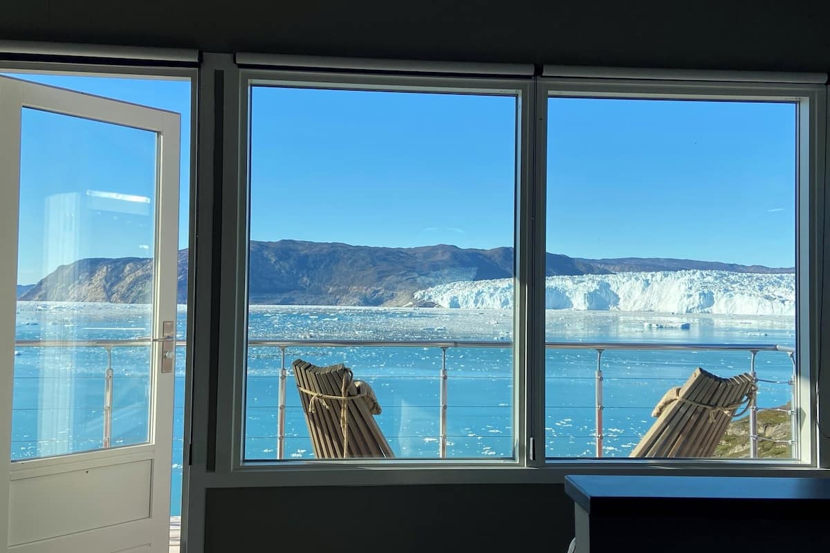 A room with large windows offering a view of a glacier and mountains.