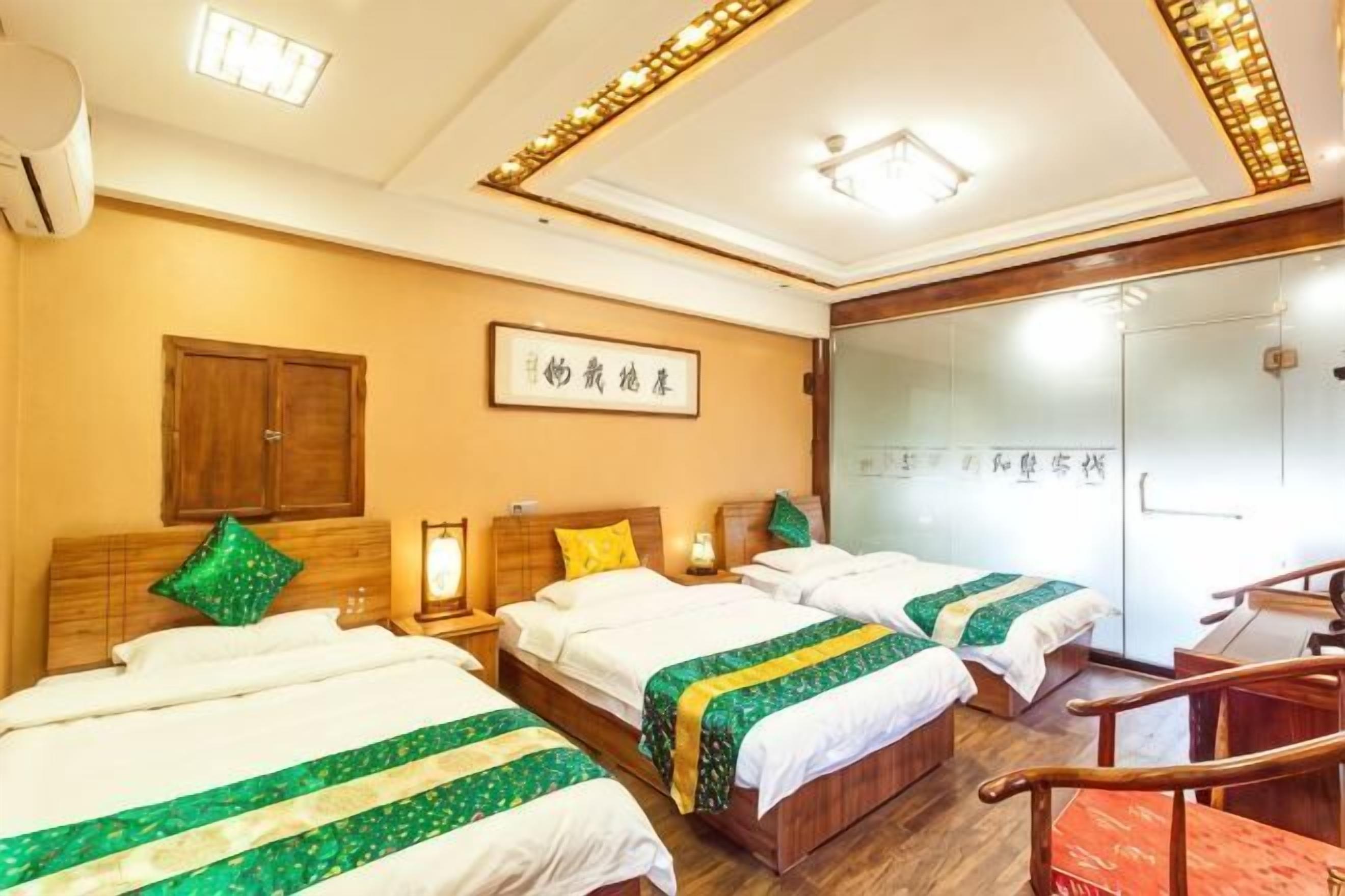 Ein Hotelzimmer mit drei Betten, Holz-Kopfteilen, einem an der Wand befestigten Fernseher und einem Schiebetürenschrank.