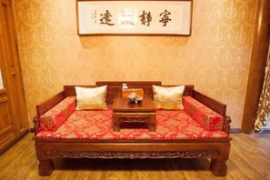 Una cama de madera tradicional con ropa de cama roja estampada y dos almohadas, una mesita de madera en frente y un cartel enmarcado en la pared.