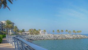 A waterfront promenade with a stone wall, palm trees, and modern buildings. - Capital Stay | 2 Bed Apt |  The Address Fujairah (Fujairah)