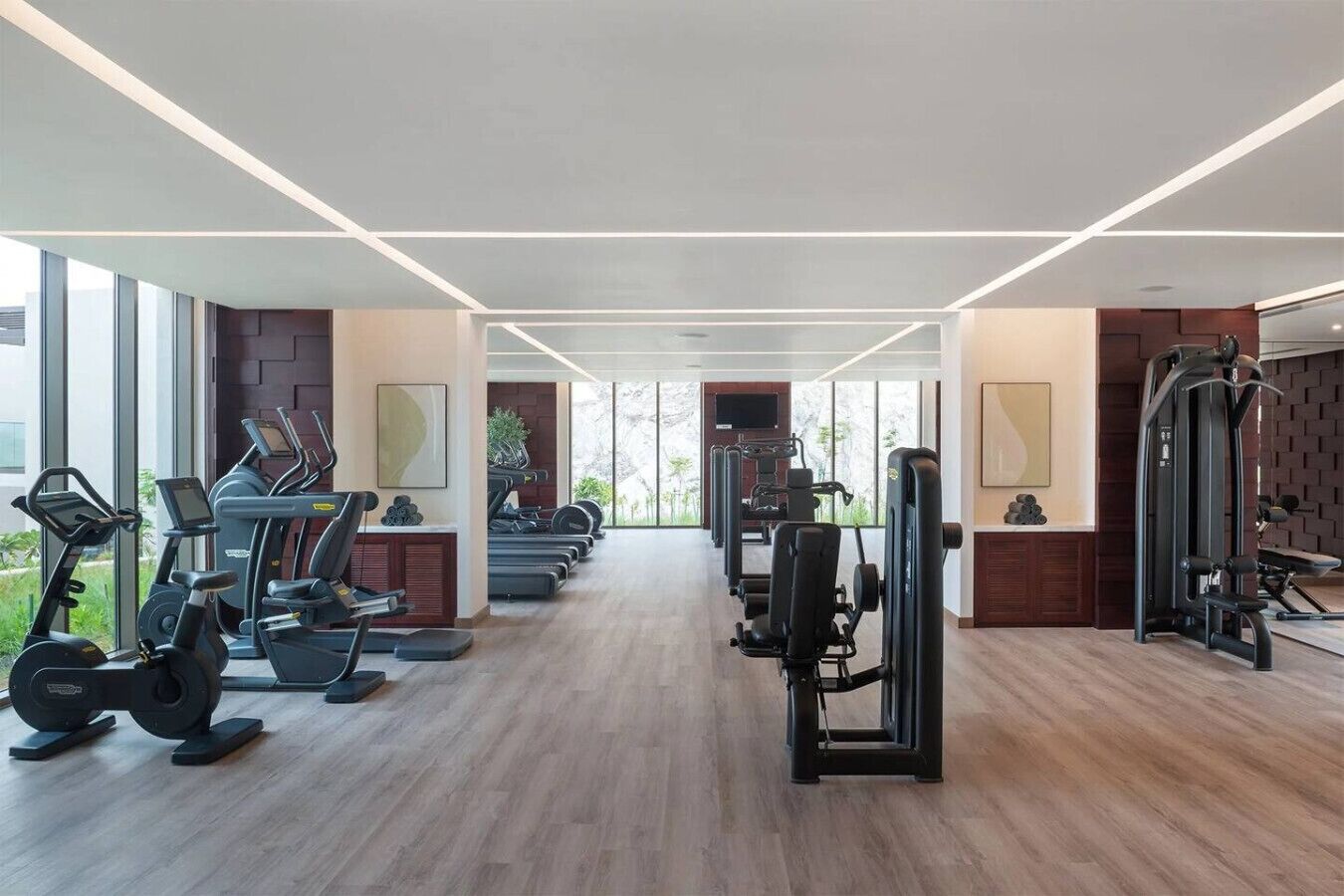 A modern gym with cardio machines, weight stations, and a large window providing natural light.