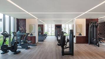 A modern gym with cardio machines, weight stations, and a large window providing natural light.