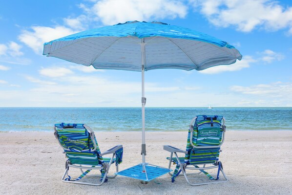 Two beach chairs under a blue umbrella on a sandy beach with the ocean in the background. - Condo Located in Goodland Just a Short Walk From Great Food (Goodland)
