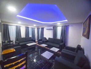 A modern living room with a black sofa set, a glass coffee table, and a black and yellow striped chair. - WAJE HOTEL (Lagos)