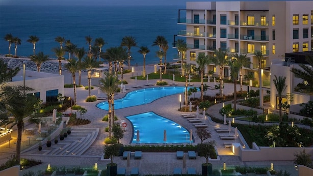 A modern hotel with a pool area, palm trees, and a view of the ocean.