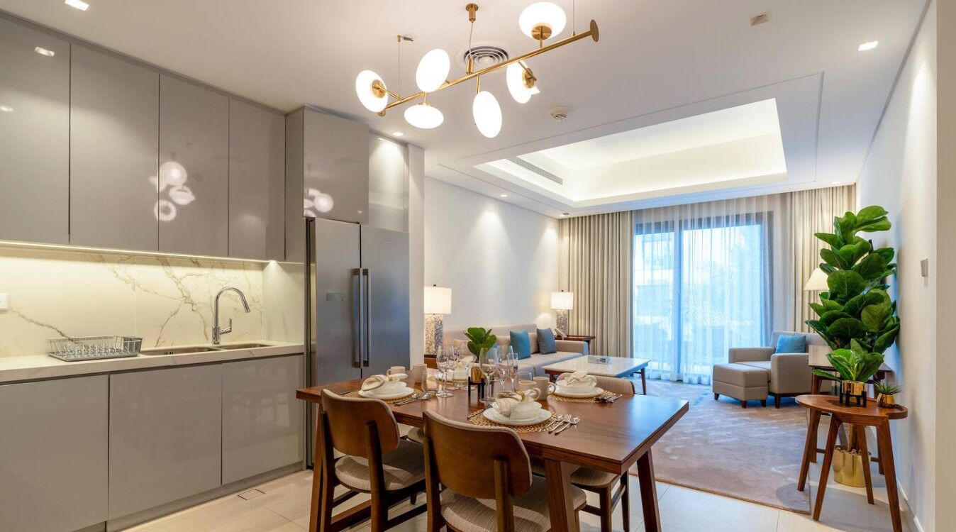 A modern kitchen with a dining area, a living room with a sofa and coffee table, and a large window with curtains.