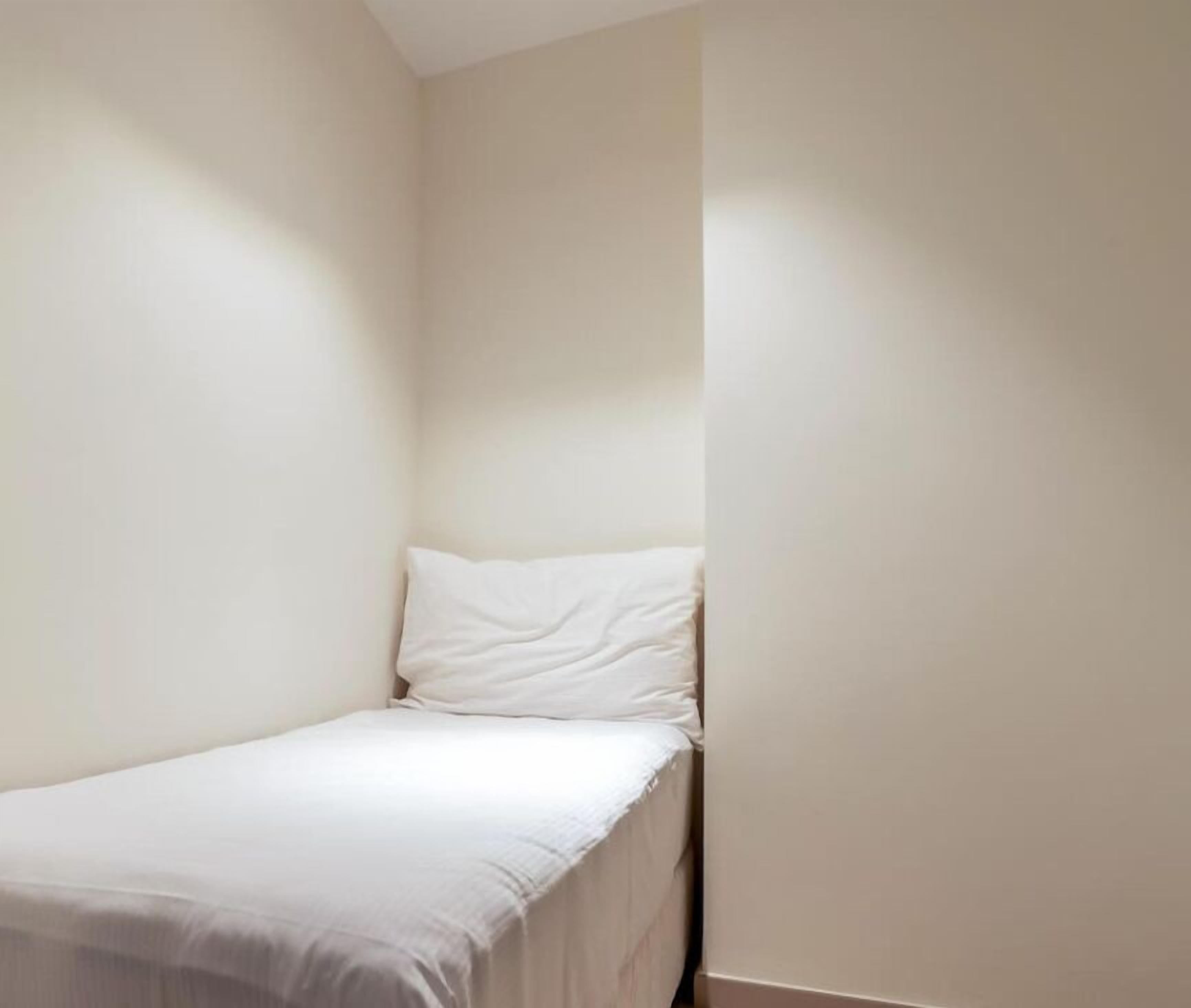A small, unadorned room with a single bed and a plain wall.