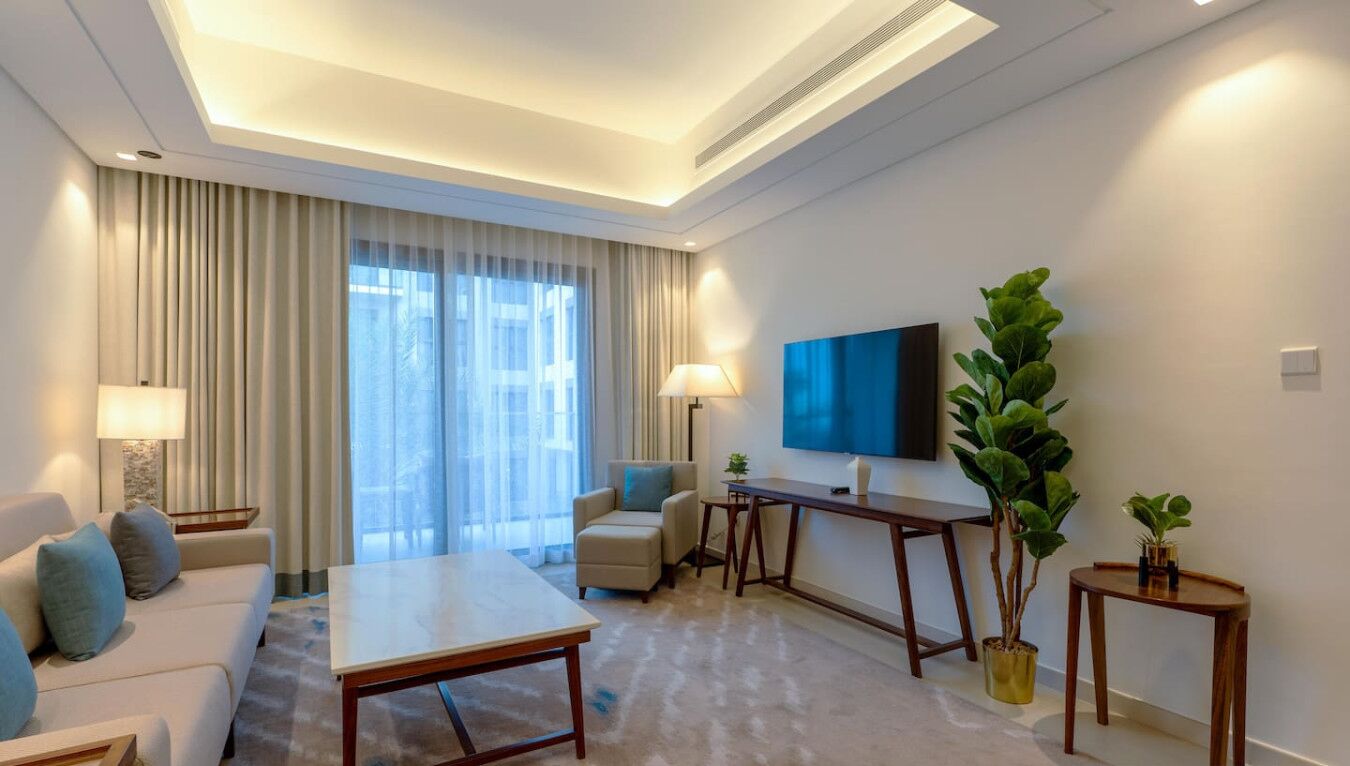 Una habitación de hotel moderna con sofá, mesa de centro, televisor y un ventanal con cortinas.