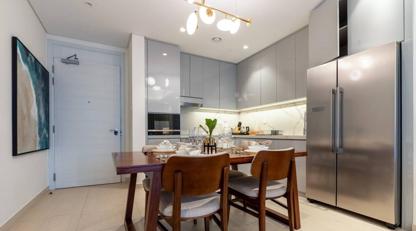 A modern kitchen with grey cabinets, a stainless steel refrigerator, and a dining area with a wooden table and chairs.