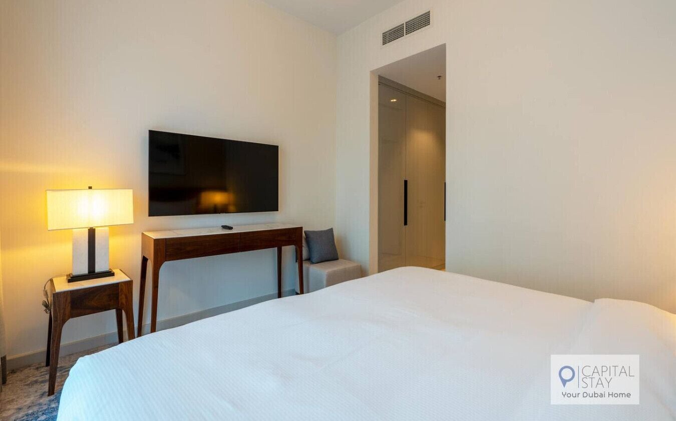 Een hotelkamer met een bed, een bureau met lamp, een televisie en een deur.