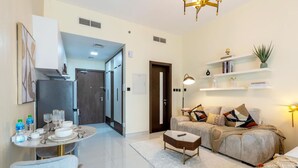 A modern living room with a sofa, coffee table, and a dining area with a table set for two. - Capital Stay - Cozy Studio in Liwan Dubai (Dubai)