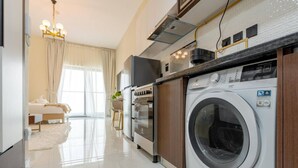 A modern kitchen with a built-in washing machine, oven, and a dining area with a table and chairs. - Capital Stay - Cozy Studio in Liwan Dubai (Dubai)