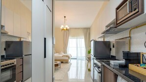 A modern kitchen with stainless steel appliances, a central island, and a view into a bedroom with a large window. - Capital Stay - Cozy Studio in Liwan Dubai (Dubai)