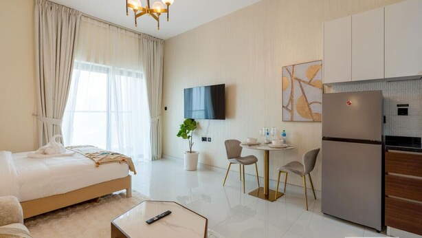 A hotel room with a bed, a small dining area with a table and chairs, a refrigerator, and a TV mounted on the wall. - Capital Stay - Cozy Studio in Liwan Dubai (Dubai)