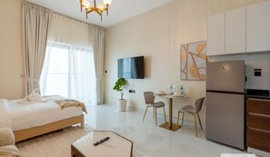 A hotel room with a bed, a small dining area with a table and chairs, a refrigerator, and a TV mounted on the wall. - Capital Stay - Cozy Studio in Liwan Dubai (Dubai)