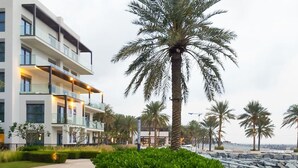 Un bâtiment moderne doté de nombreux balcons et d’un jardin bien entretenu agrémenté de palmiers.