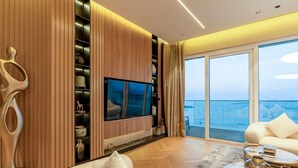 Een moderne woonkamer met een grote flatscreen televisie, houten lambrisering, een bank en uitzicht op zee door grote ramen.