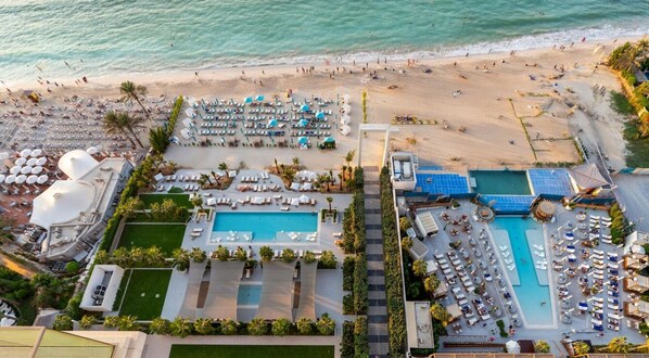 An aerial view of a beach resort with multiple swimming pools, sun loungers, and a beach area.