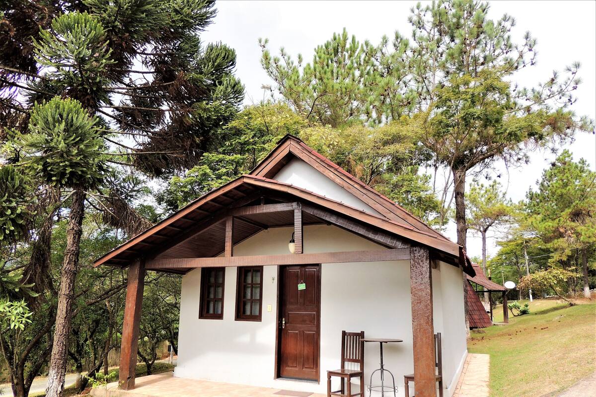 A small, single-story building with a sloped roof, a front door, and a small porch with two chairs and a table.
