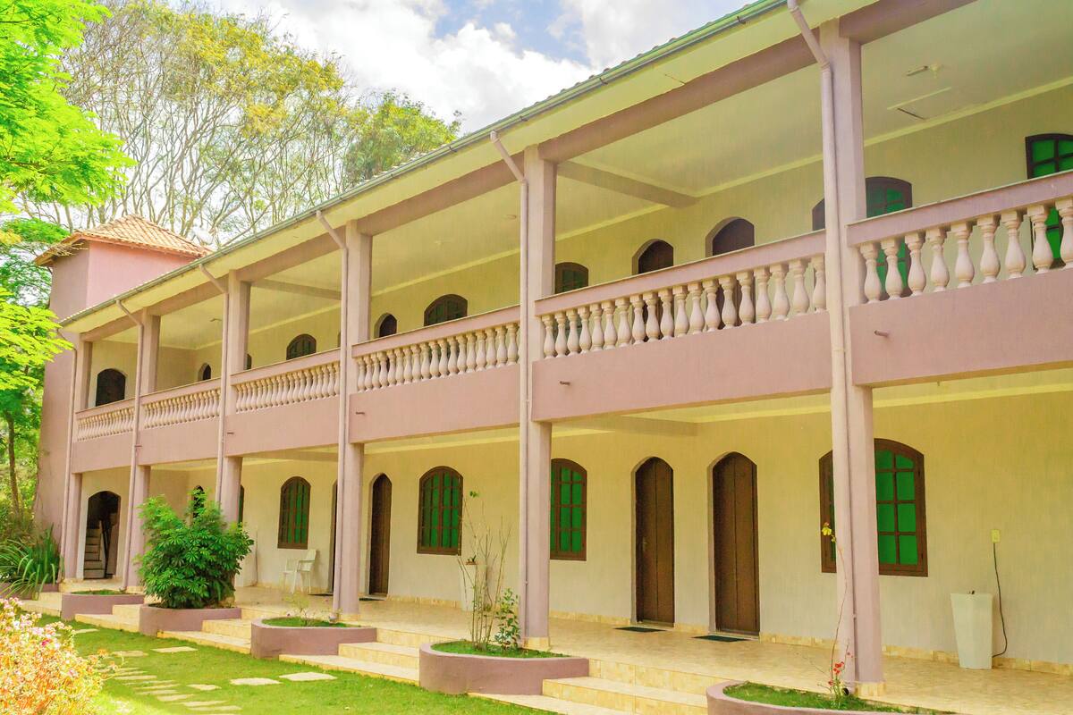 A two-story building with a covered balcony, multiple windows, and a garden area.