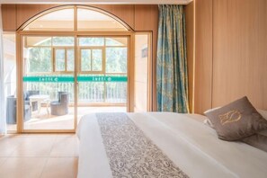 Habitación de hotel con cama, vista al balcón exterior y una puerta de madera.