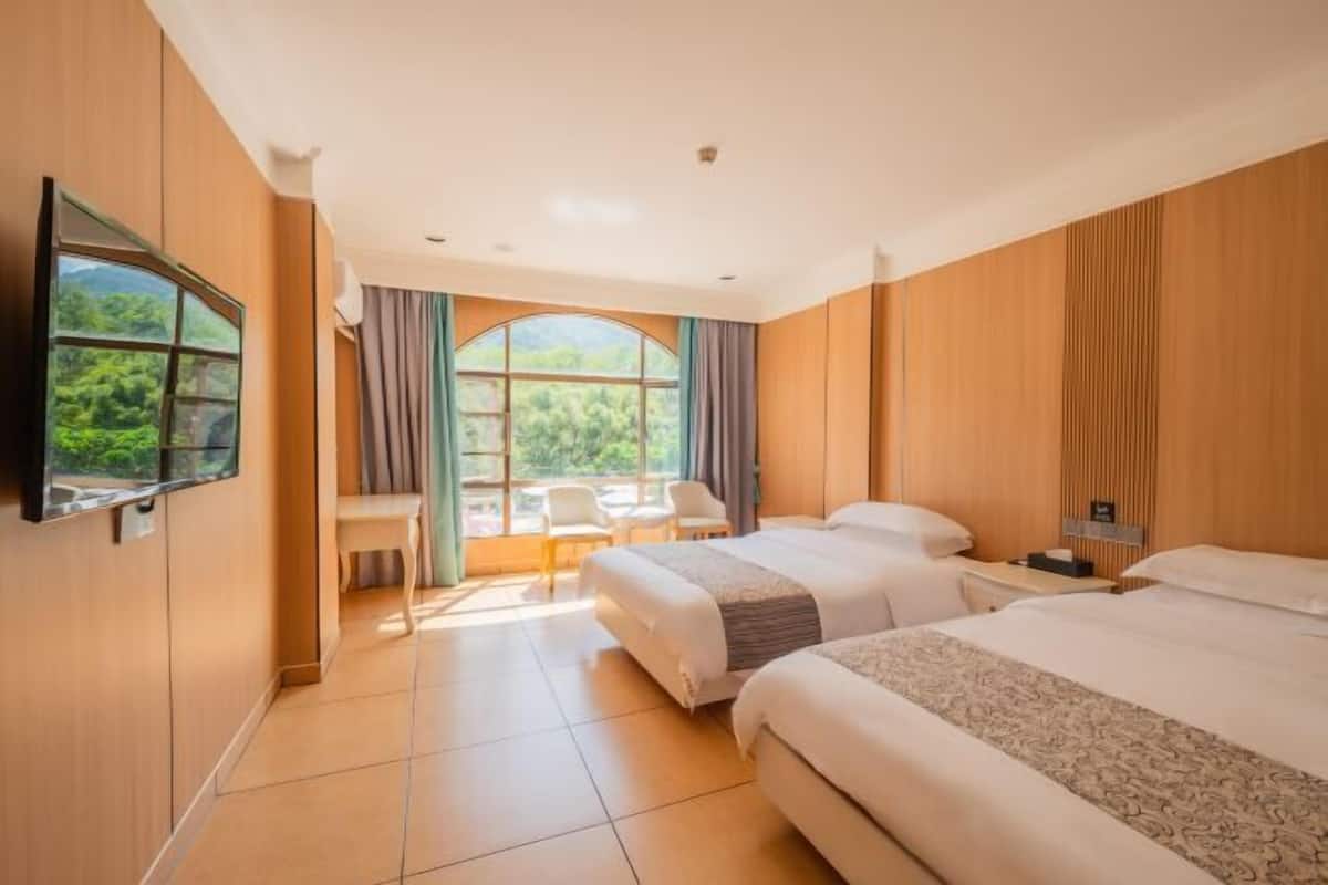 A hotel room with two beds, a TV, a desk, and a window with curtains.