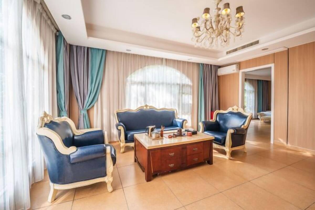 A room with a chandelier, two blue sofas, a wooden coffee table, and curtains.