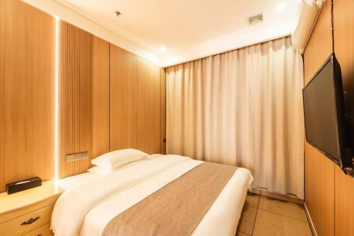 A hotel room with a bed, a bedside table, a TV, and a curtain.