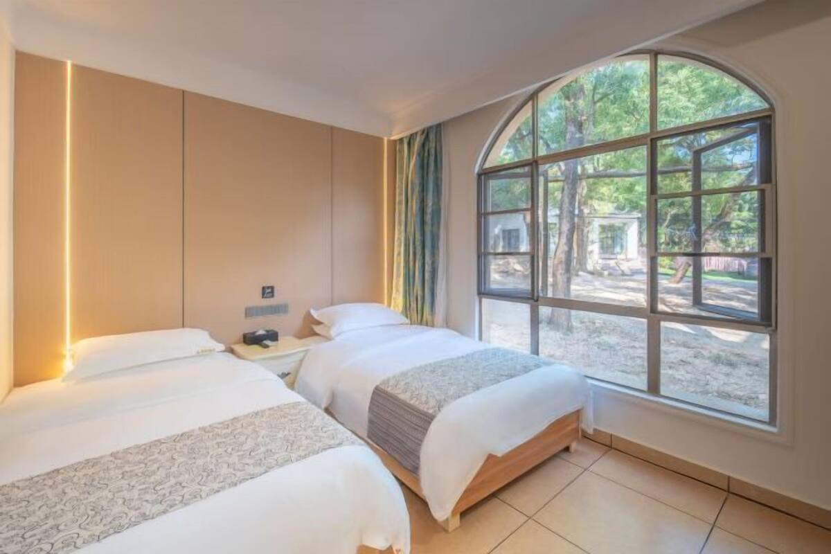 A hotel room with two beds, a large arched window, and a view of the outdoors.
