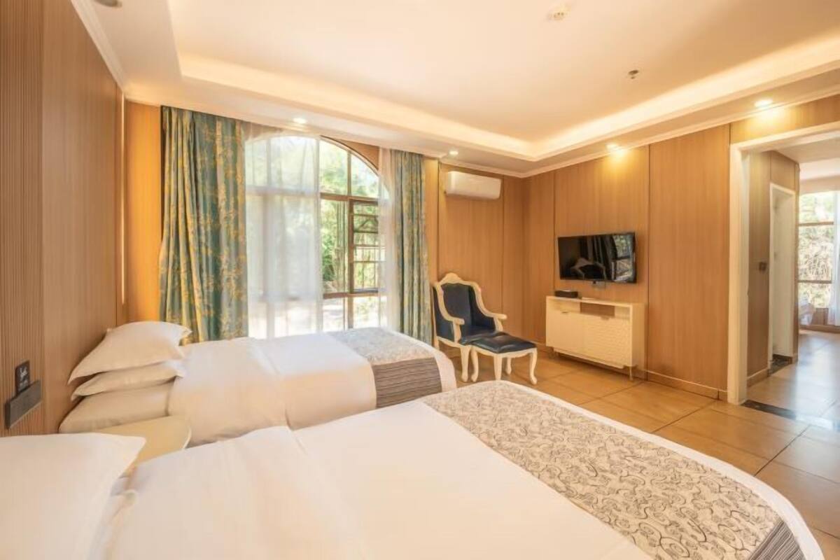 A hotel room with two beds, a desk, a chair, and a TV.