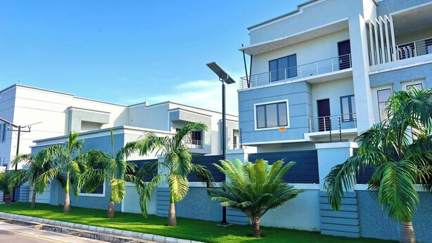 A modern residential building with a flat roof, multiple balconies, and a well-maintained lawn with palm trees. - CITY DEN APARTMENT (Kaduna)