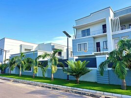 Um edifício residencial moderno com telhado plano, várias varandas e um gramado bem cuidado com palmeiras.