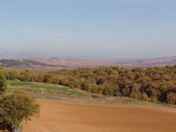 A rural landscape with a dirt field, a golf course, and dense forested hills in the background. - Apartamento Dúplex Golf Rioja Alta (Cirueña)