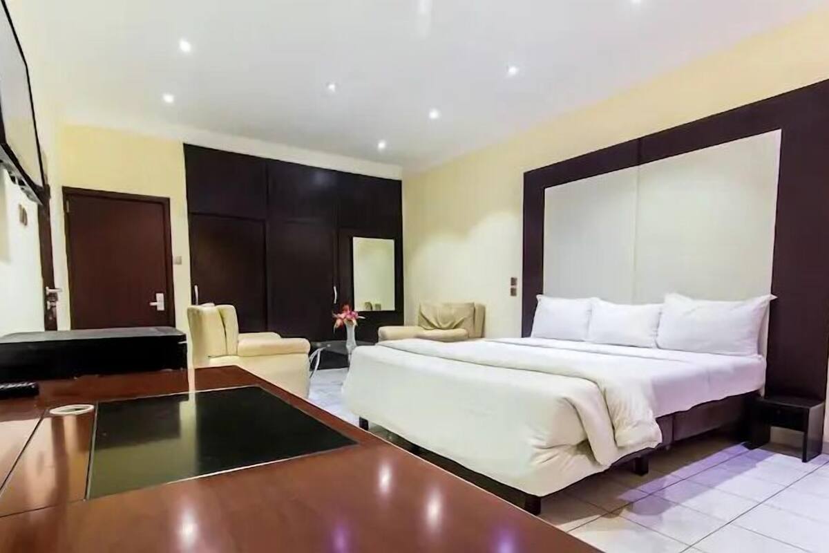 A modern hotel room with a large bed, a desk, a chair, and a sofa.