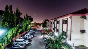 Um estacionamento com vários carros estacionados em frente a um edifício com telhado vermelho e paredes brancas.
