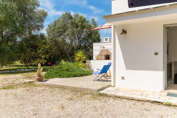 A white building with a covered patio, a blue chair, and a cactus in a pot.