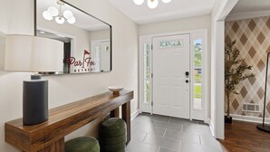 Un couloir moderne avec une console en bois, un miroir et une porte donnant sur l’extérieur.