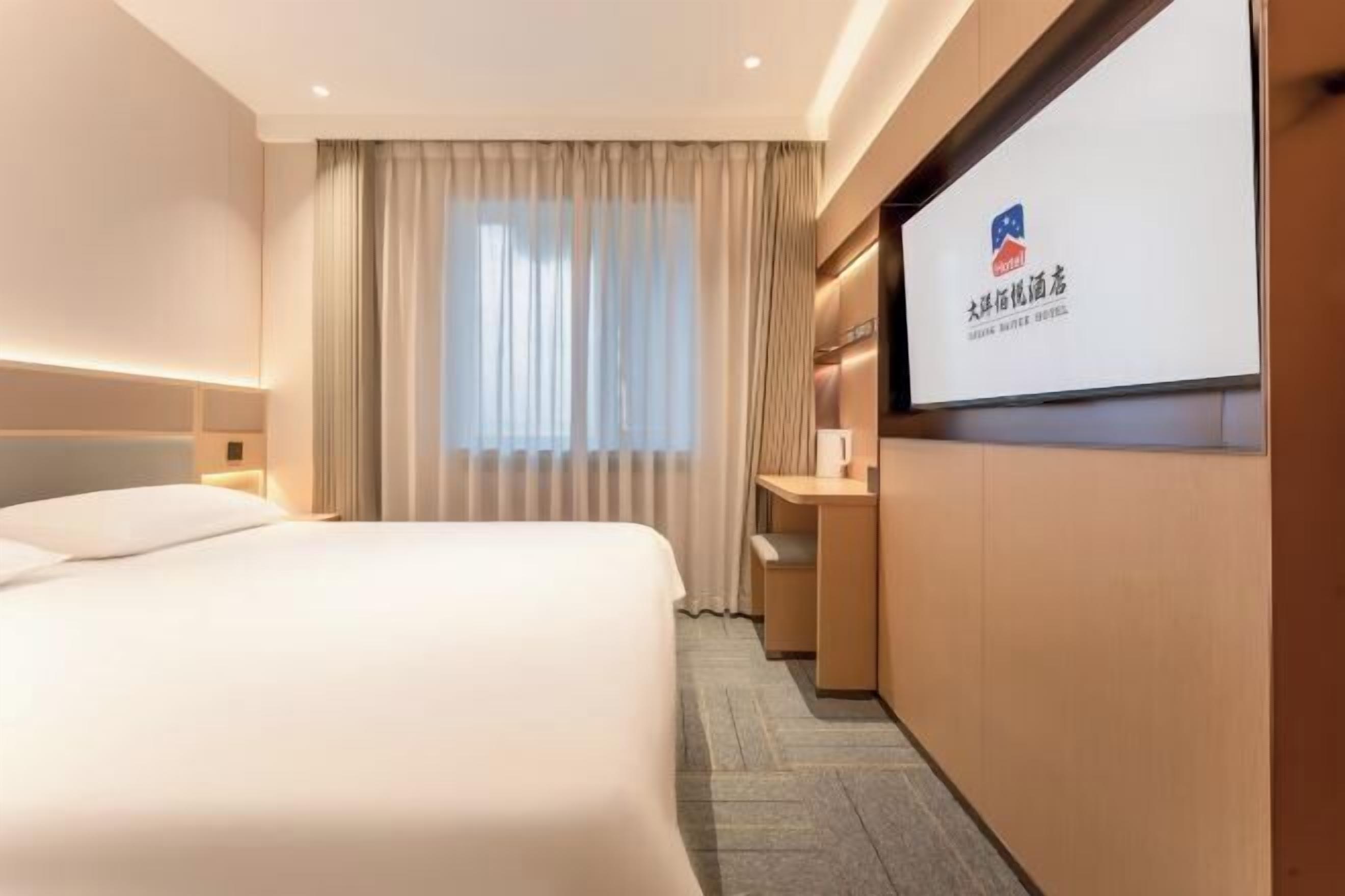 A hotel room with a bed, a desk, a TV screen, and a window with curtains.