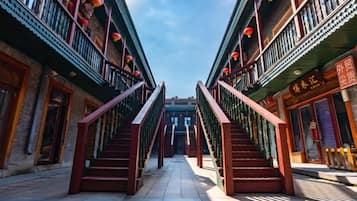 A traditional courtyard with a central staircase flanked by buildings with balconies and red lanterns.