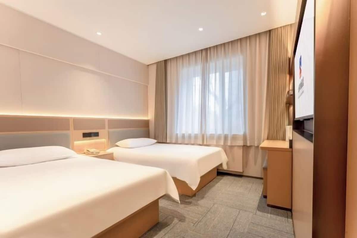 Ein Hotelzimmer mit zwei Betten, einem Schreibtisch, einem Fernseher und einem großen Fenster mit Vorhängen.