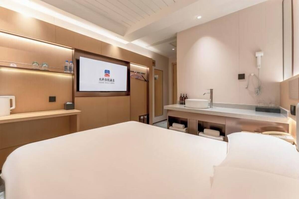 Ein Hotelzimmer mit Bett, Fernseher, Minibar und einem Badezimmer mit Waschbecken und Spiegel.